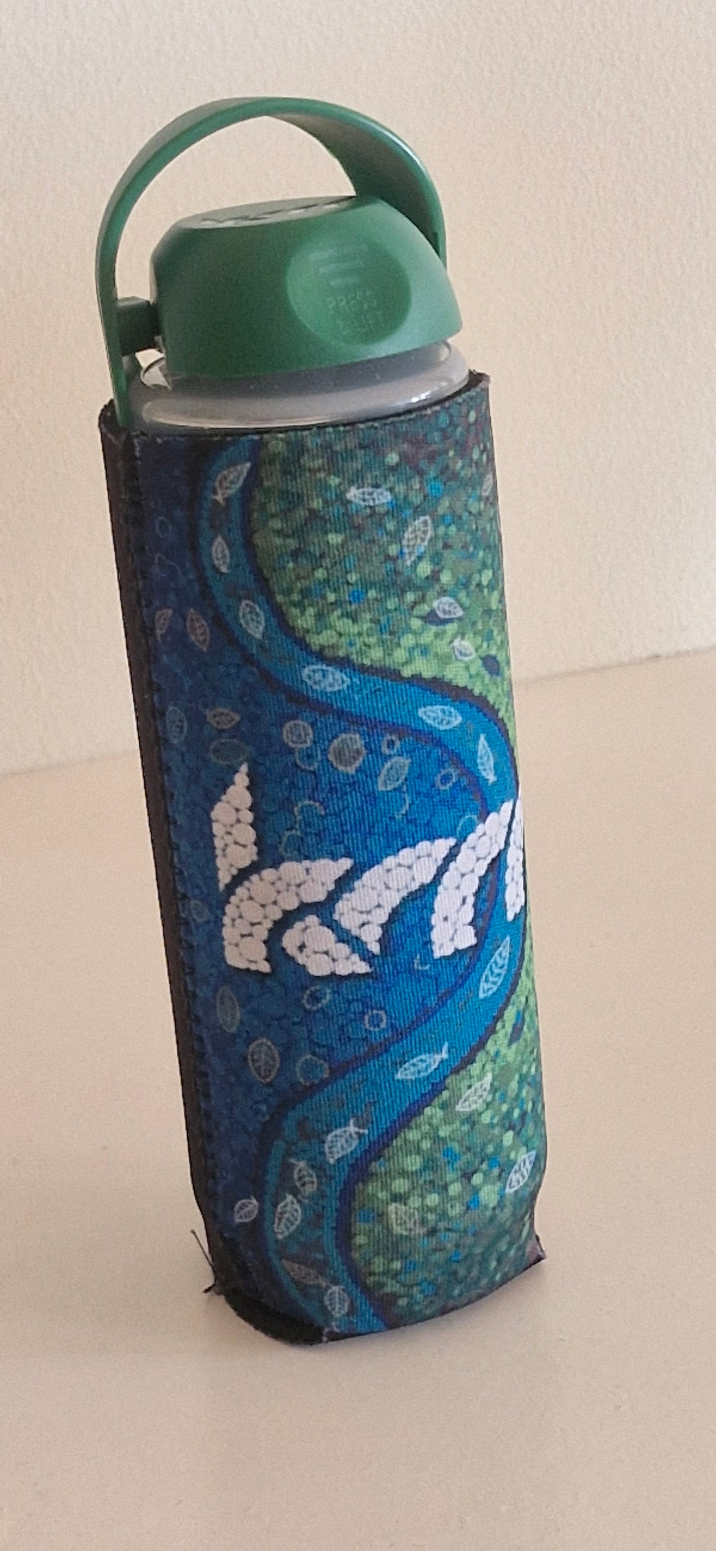 Koor Bottle with a decorative cover featuring a blue and green pattern on a beige background